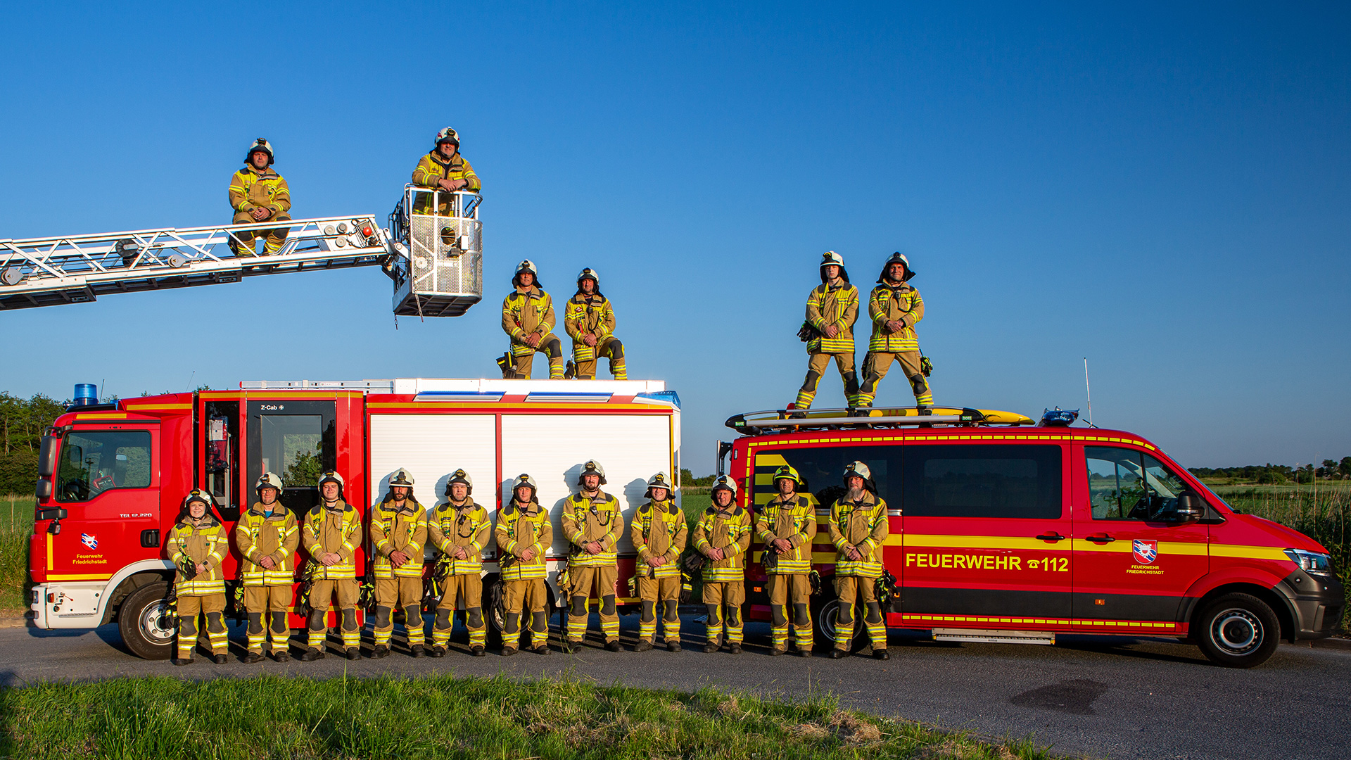 Feuerwehrmannschaft vor ihren Einsatzwagen und auf dem Feuerwehrkran