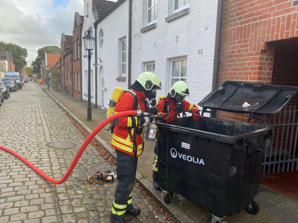 Feuerwehrleute löschen eine brennende Mülltonne in der Altstadt von Friedrichstadt